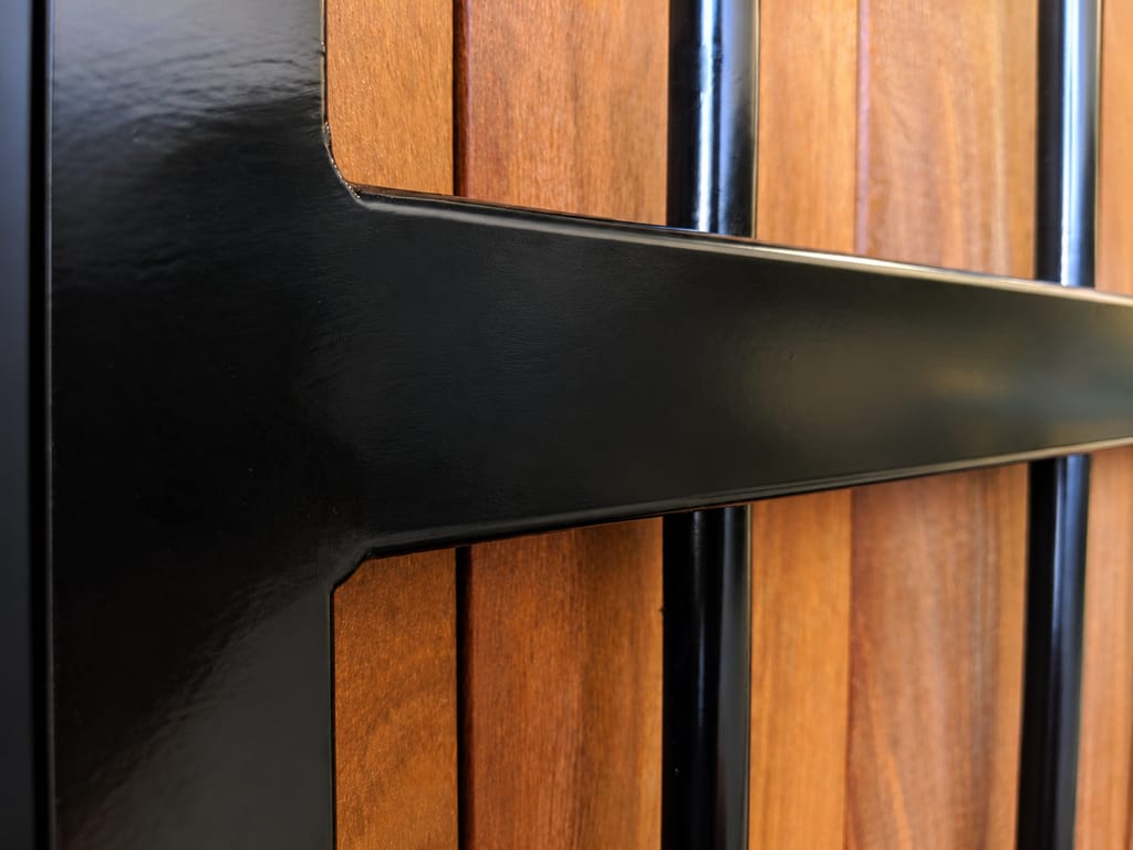 Close-up of a GateFrames luxury fence panel: black steel rail and round pickets over vertical ironwood