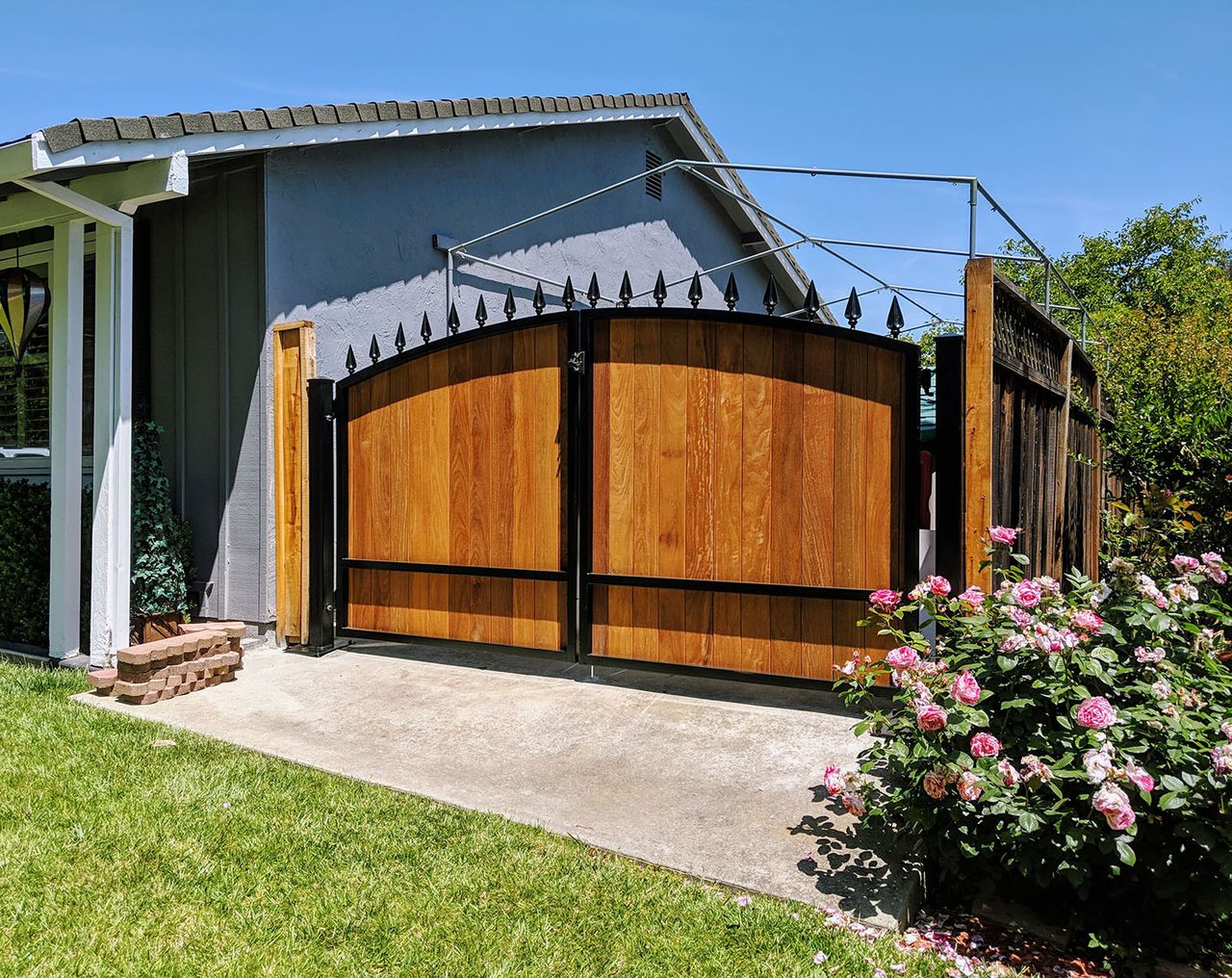 Arched black steel driveway gate with vertical wood infill and spear finials