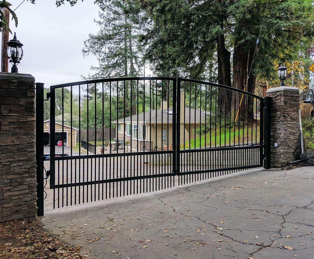 Black steel center-opening driveway gate with puppy pickets and an arched top