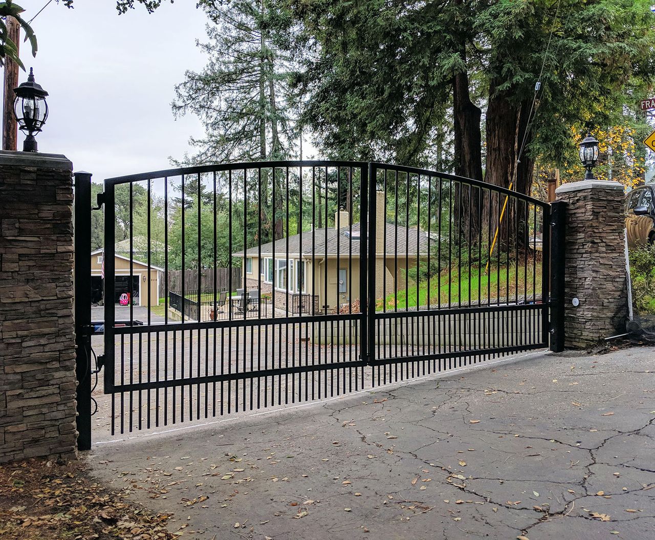 Arched black steel double driveway gate with open upper pickets and close-set lower pickets